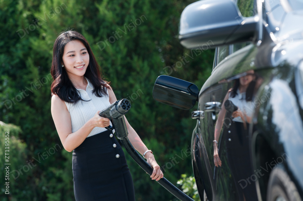 青年女人拿着充电枪准备给汽车充电图片