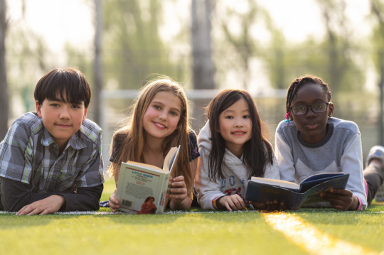 可爱的小学生们趴在草地上看书