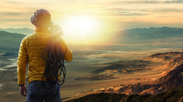 青年登山者扛着绳索站在山顶