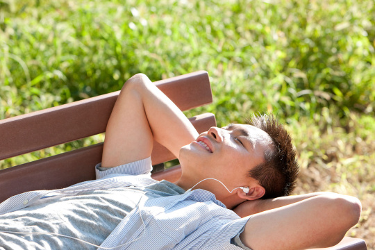 青年男子躺在公园长凳上听音乐