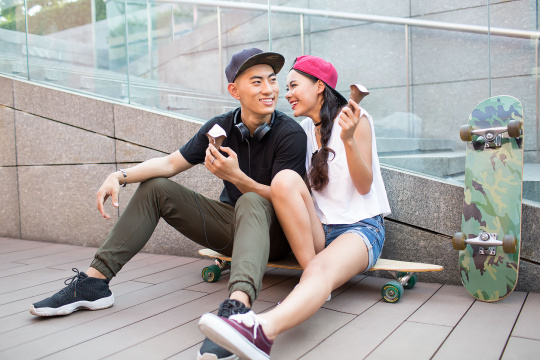 快乐的年轻情侣坐在滑板上吃冰淇淋