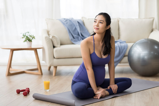 年轻孕妇坐在瑜伽垫上思考