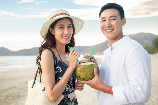 快乐的年轻情侣在沙滩喝椰汁