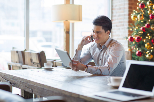 年轻男子在咖啡馆边打电话边使用平板电脑