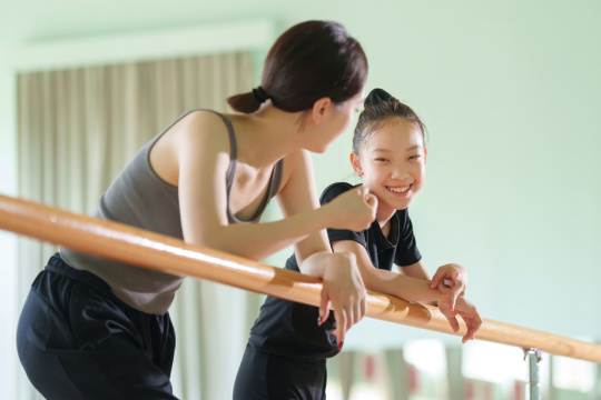 年轻的体操教师和女孩趴在把杆上聊天