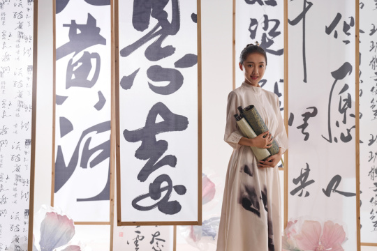 一位中国古装美女拿着卷轴站在书法作品前