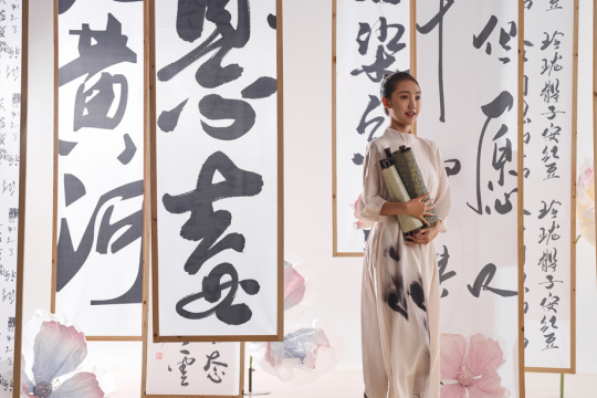 一位中国古装美女拿着卷轴站在书法作品前
