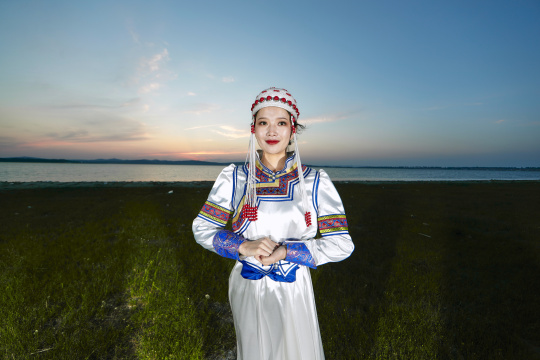 晚霞的草原湖畔穿蒙古族传统服饰的年轻女性