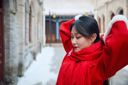 雪后在老城古巷穿着喜庆服饰的亚洲少女
