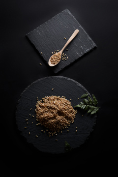 黑色青石板上的木质勺子装的燕麦米摆放在黑色背景中