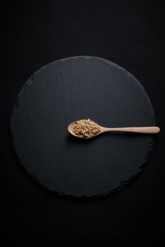 黑色青石板上的木质勺子装的燕麦米摆放在黑色背景中