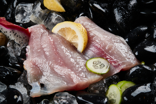 将晶莹白润的鲜鱼片码放在黑色的圆瓷盘上