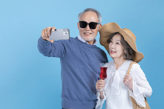 退休后的旅行 - 看着智能手机、喝着葡萄酒并比“V”字手势的老年人照片图像 