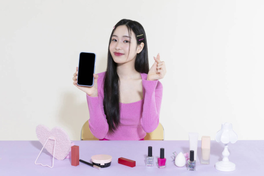 Y2K 生活方式——女子坐在梳妆台前，手持手机比心 