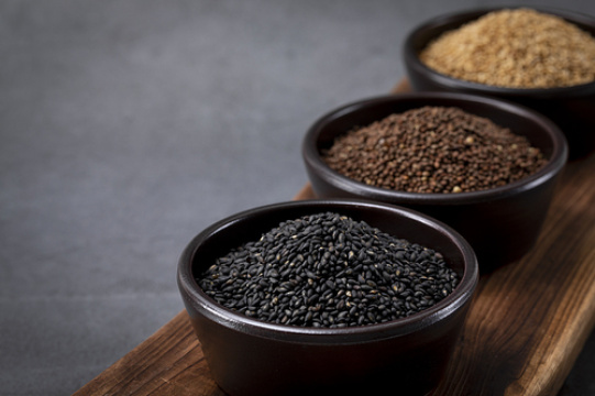 芝麻 - 陶瓷碗中装着的芝麻、紫苏籽和黑芝麻，放置在木制切菜板上 