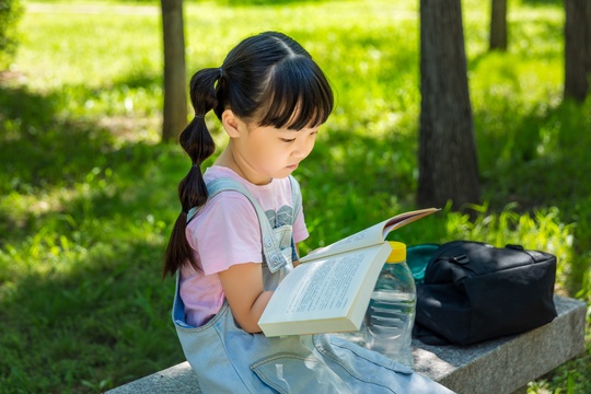 坐在公园里看书的亚洲小女孩