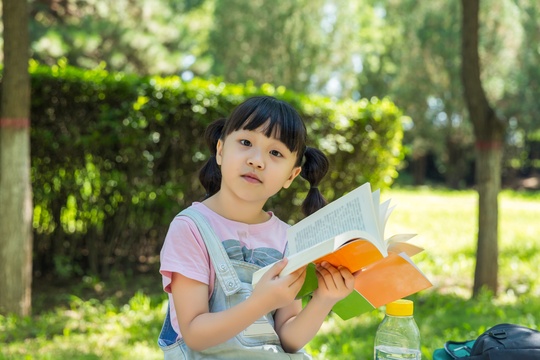 坐在公园里看书的亚洲小女孩