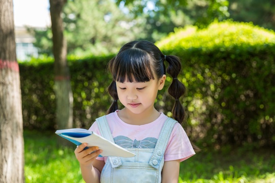 坐在公园里看书的亚洲小女孩