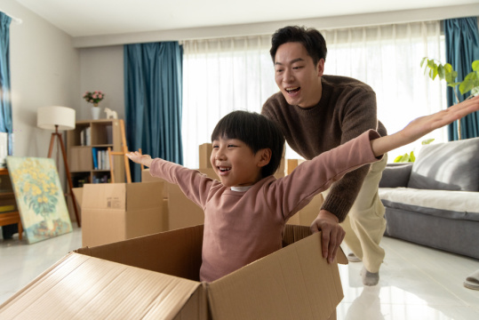 一位可爱的男孩在父亲的陪伴下在纸箱里玩耍