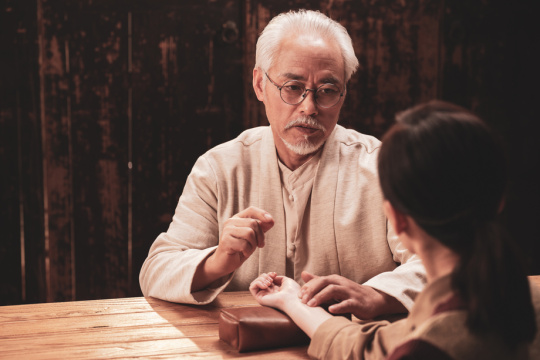 一位亚裔老年中医给患者号脉诊断病情