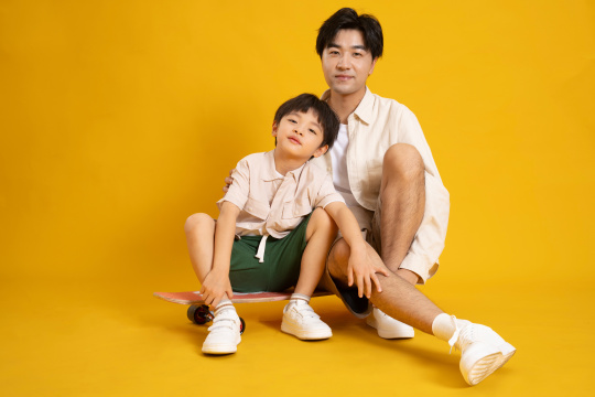 与父亲肩并肩坐在滑板上的年轻小男孩