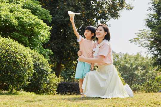 在草坪上互动玩纸飞机的母子