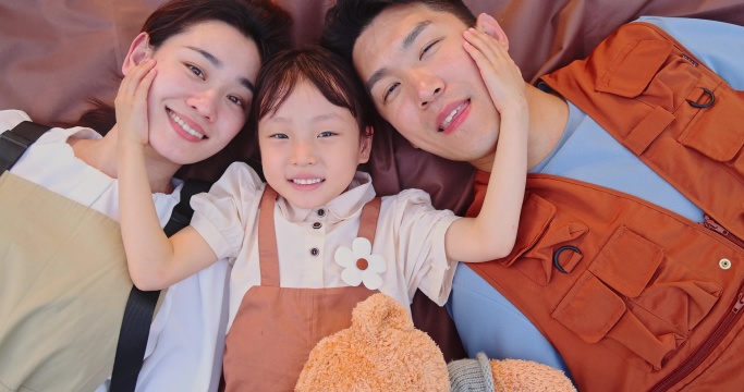 一家三口躺在野餐垫上微笑看镜头